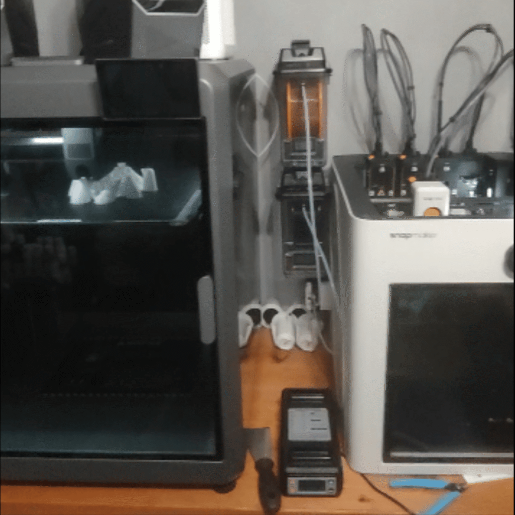 MultiForge Lab founder, a former process engineer, at his home 3D printer setup with two printers and filament dryers running side by side